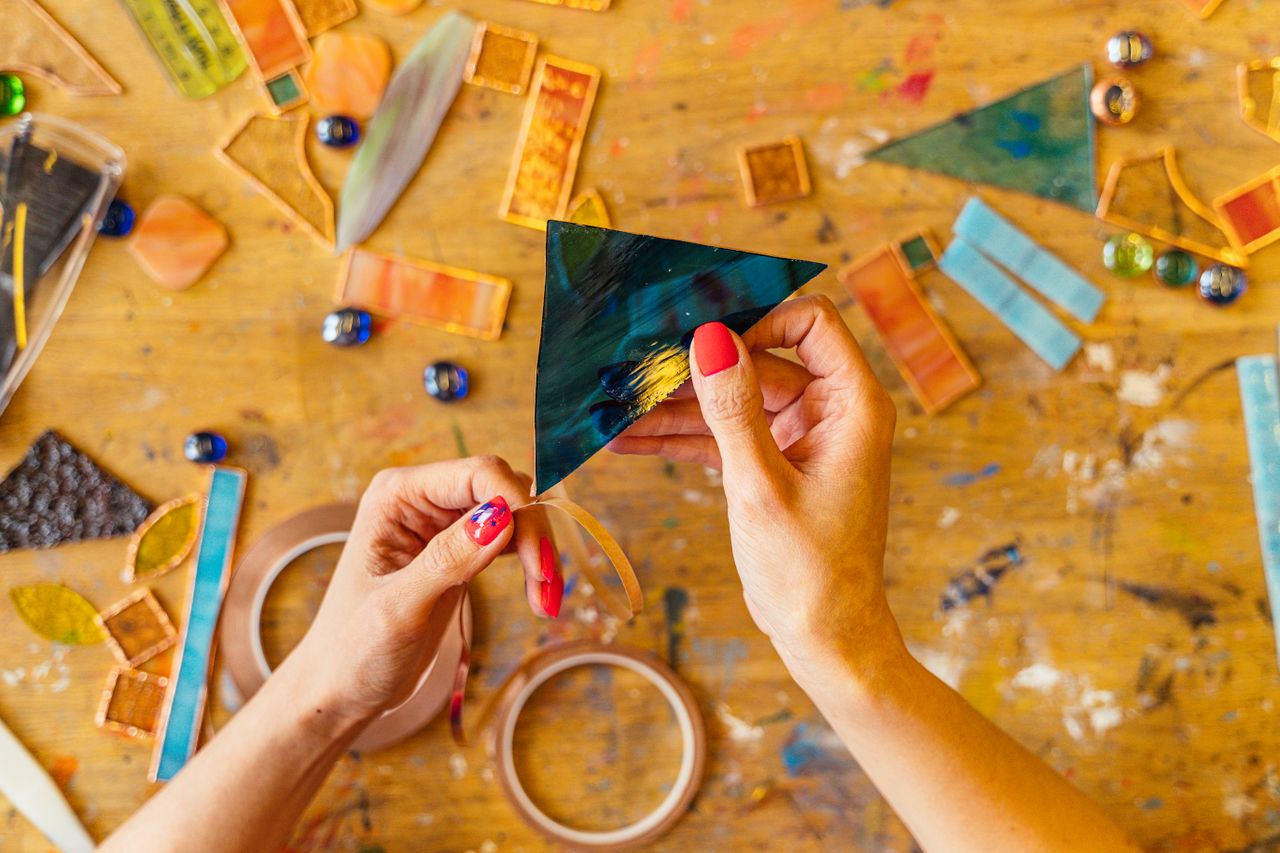 services-03 Hands crafting stained glass art with colorful pieces on a wooden table.